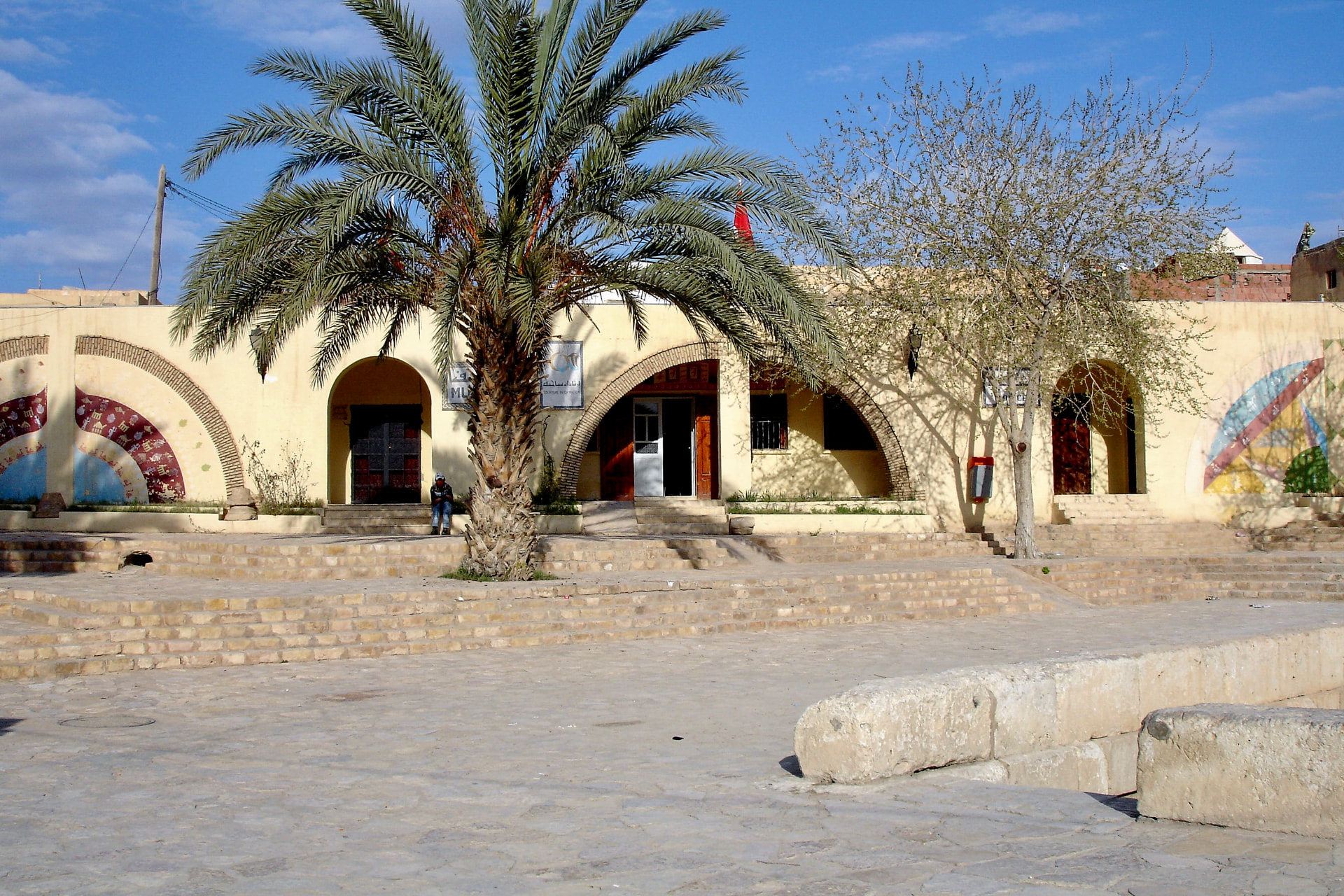 Sandfarbene Fassade mit Rundbögen und hoher Dattelpalme