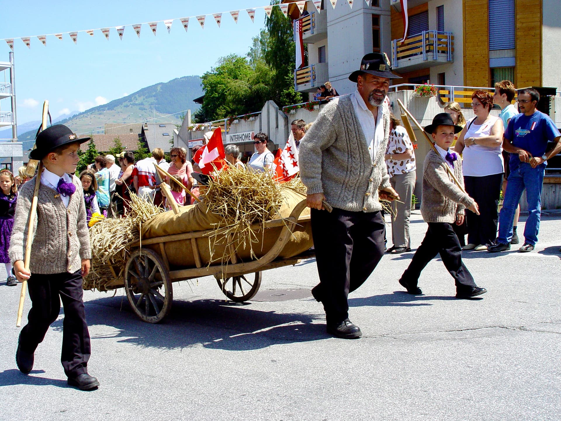 Mit Stroh und Getreidesäcken beladener Holzwagen, begleitet von Jungen mit Dreschflegeln